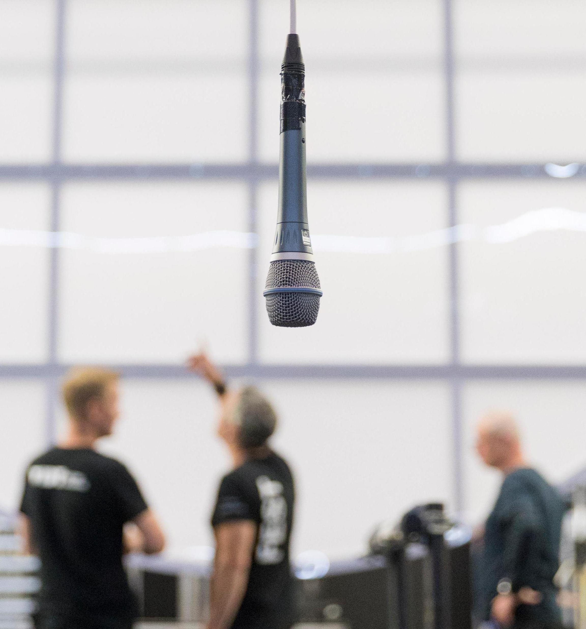 A microphone hanging down can be seen in the foreground. Several technicians are blurred in the background.