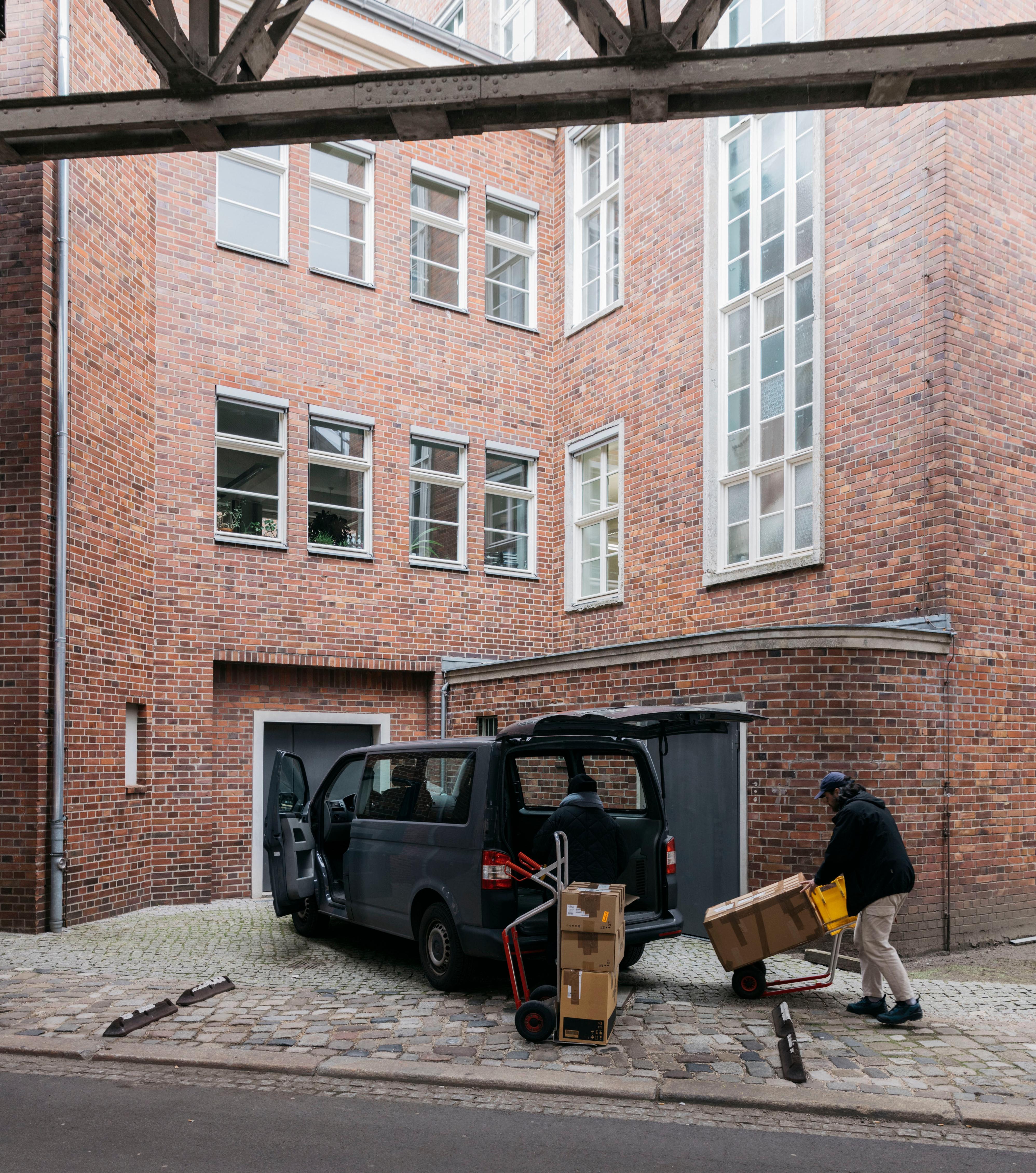 Two logistics employees loading the van. In the background is a red brick building.