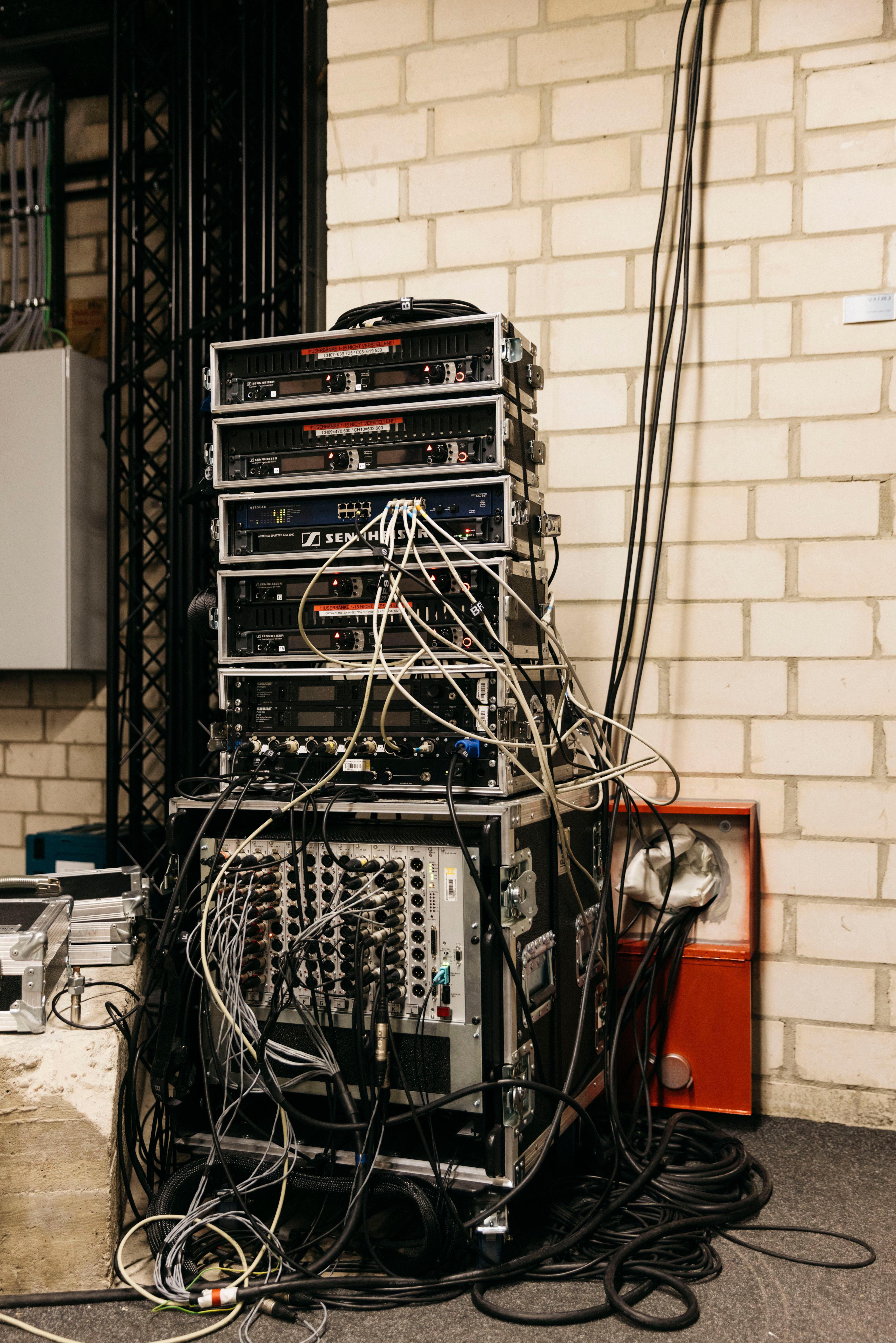Ein Server vor einer Backsteinwand. Es führen mehrere Kabel von der Wand zum Server.
