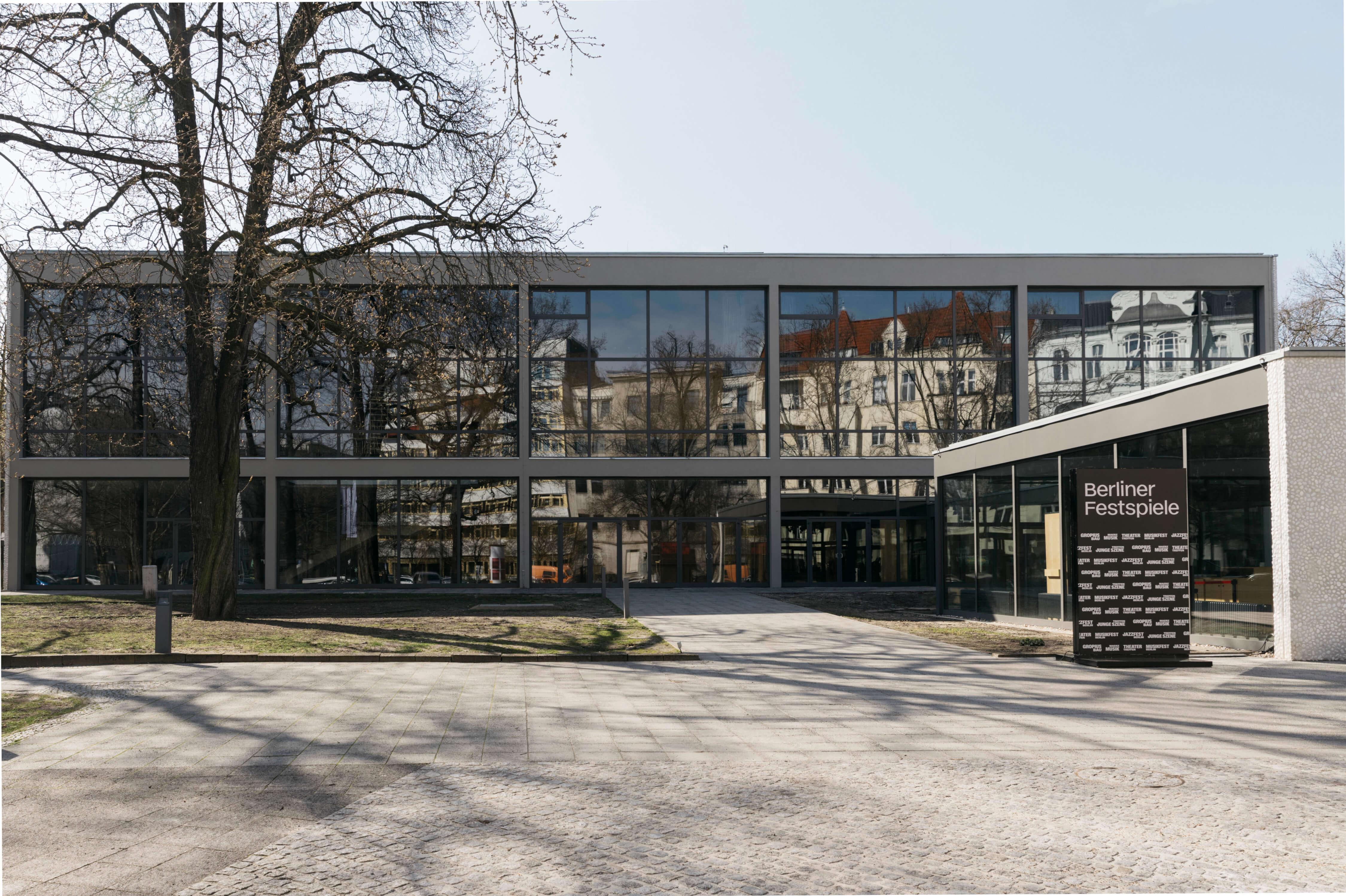 Frontal view of the Haus der Berliner Festspiele. The large glass façade of the front building can be seen.