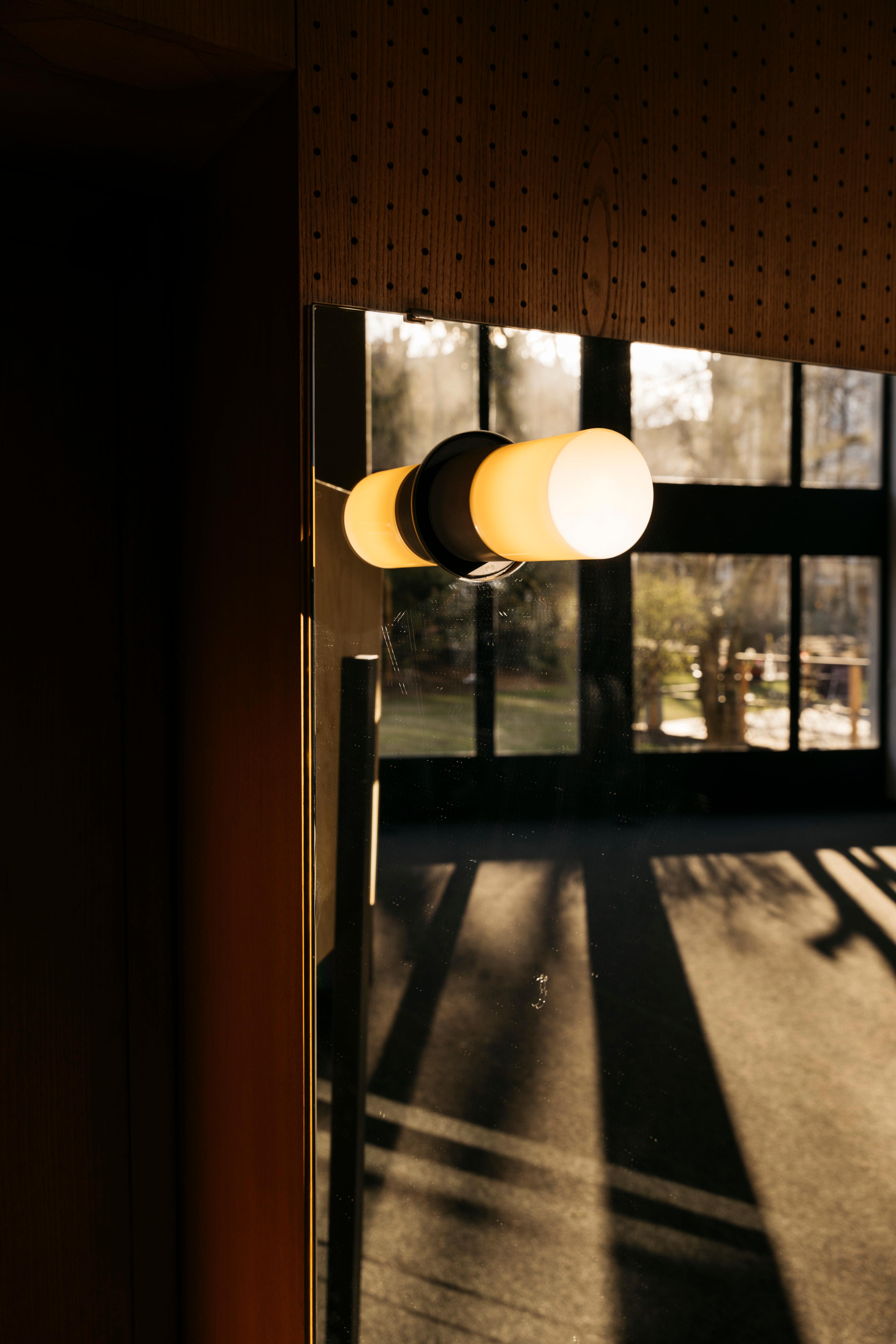 A luminous 1960s style wall lamp in front of a mirror.