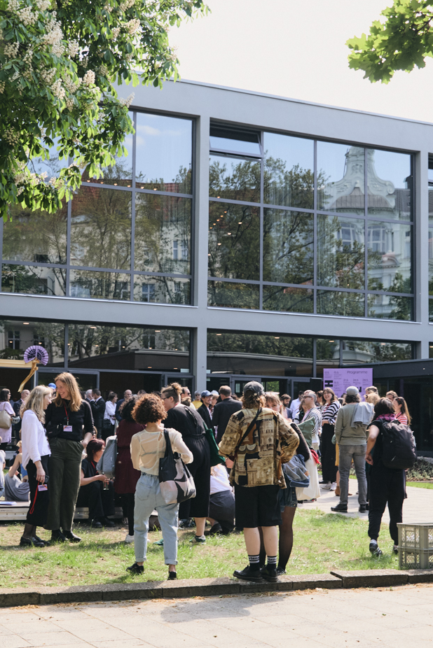 Menschen stehen auf der Wiese vor der Glasfassade des Haus der Berliner Festspiele.