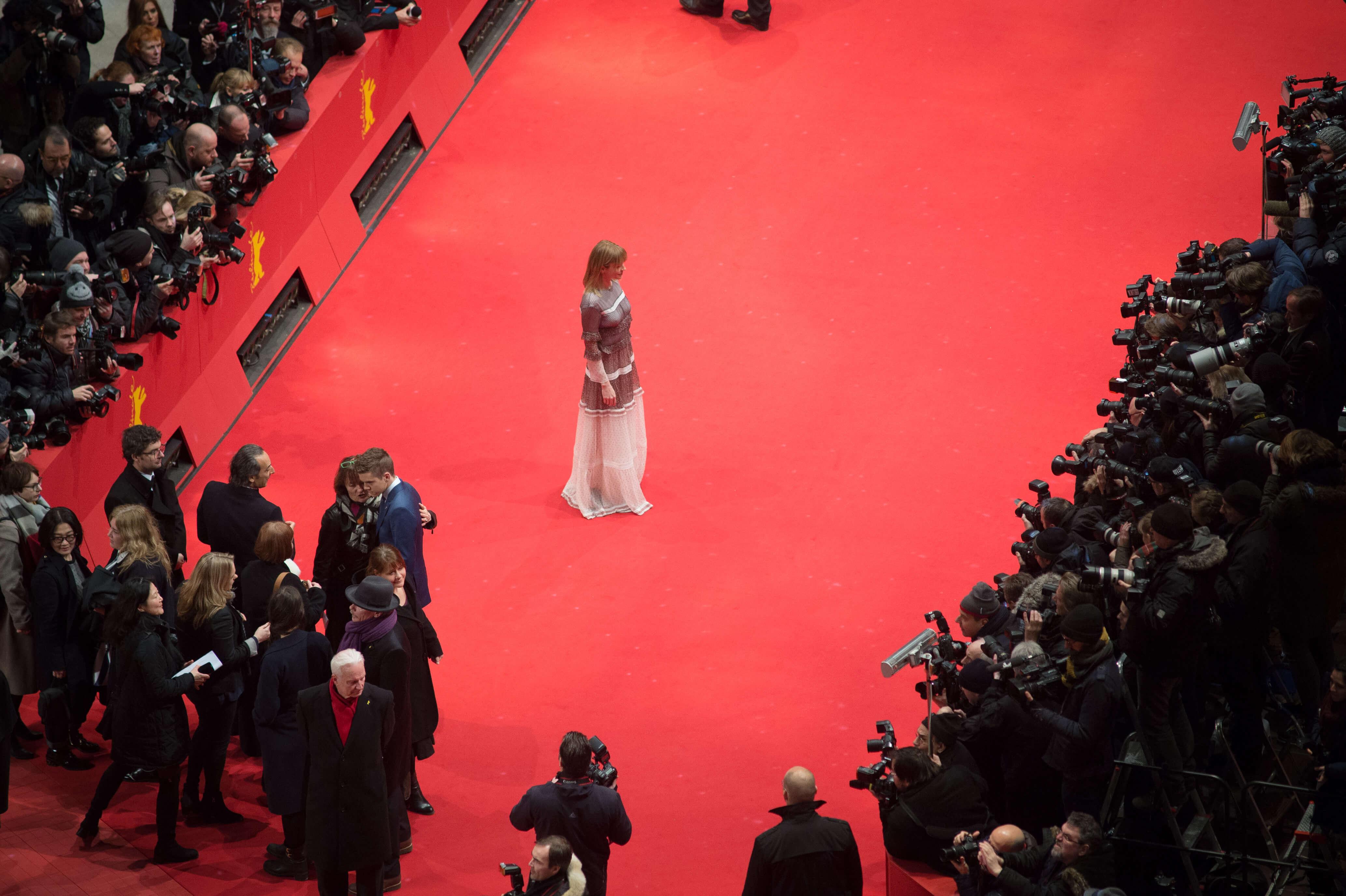 A female read on the Red Carpet. In front of and behind her are photographers.