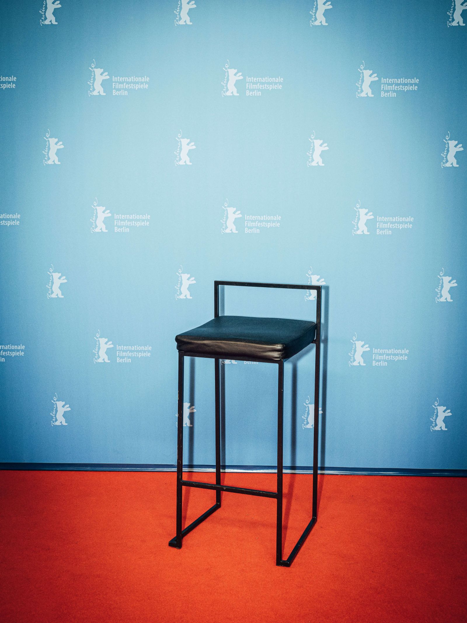Schwarzer Hocker auf rotem Teppich vor blauer Wand mit Berlinale-Logo.